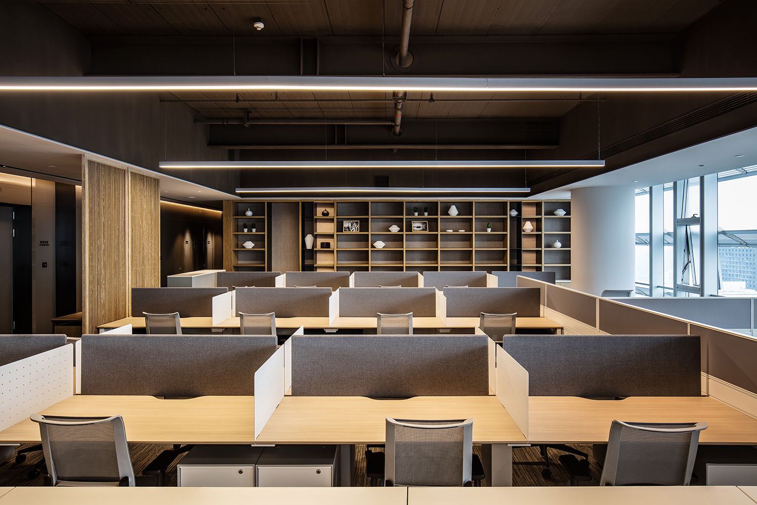 Modern corporate workstation area with linear lighting and bookshelf wall